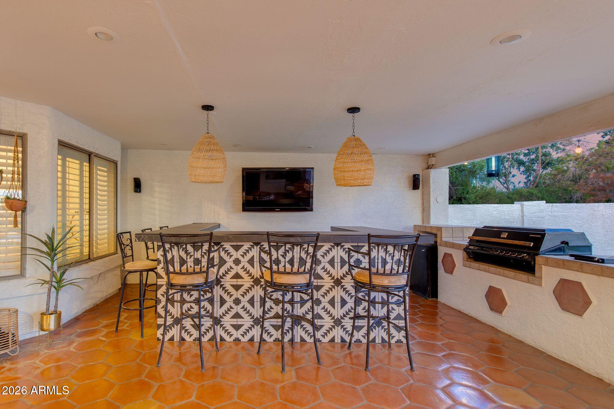 Covered patio with a patterned-tile bar, bar stools, built-in grill, and wall-mounted television.