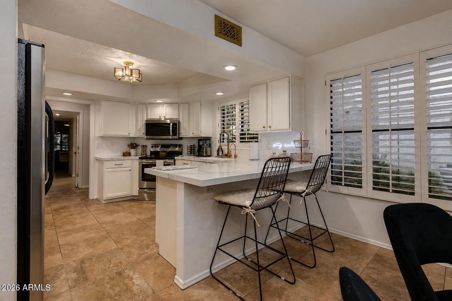 Kitchen with a large breakfast bar island, white cabinets, stainless appliances, and plantation shutters.