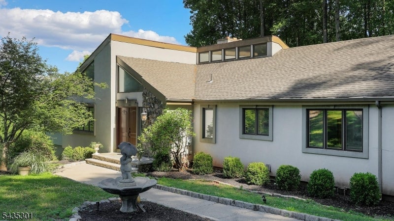 Modern gray home with angular rooflines, landscaped front yard, and a fountain beside the walkway.