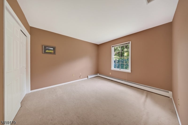 Vacant carpeted bedroom with tan walls, a window, and white baseboard heating.