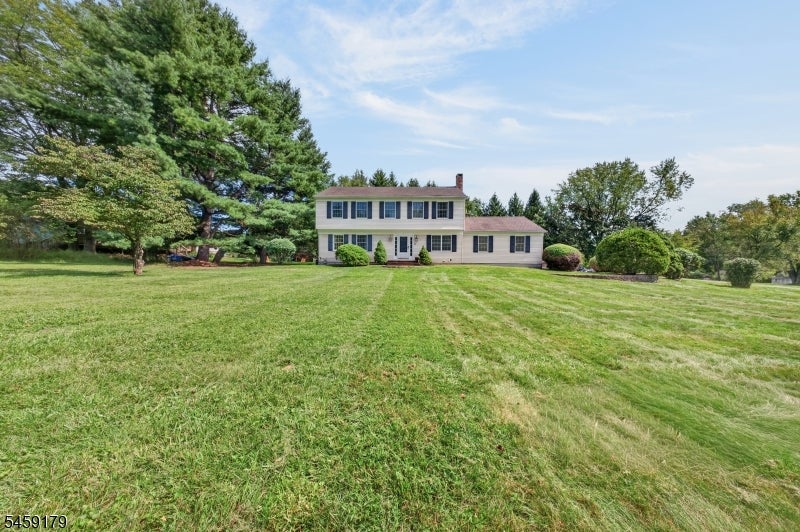 Two-story house beyond a broad lawn, framed by mature trees and shrubs.