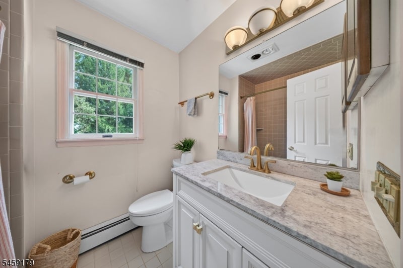 Bathroom with a white vanity, brass faucet, large mirror, and window overlooking trees.