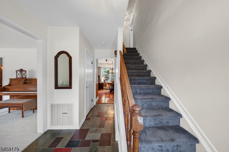 Foyer with slate tile flooring and a carpeted staircase with wooden banister.