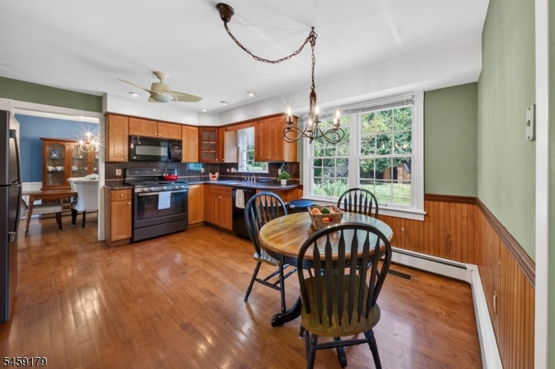 Kitchen and dining area with wood cabinetry, black appliances, and a round table beside a large window.
