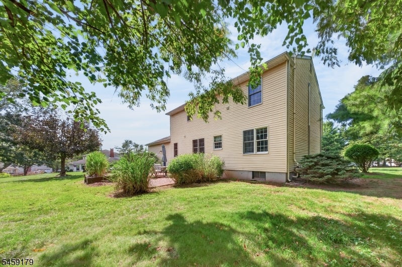 Beige two-story house viewed from the side, with a small patio and landscaped lawn.