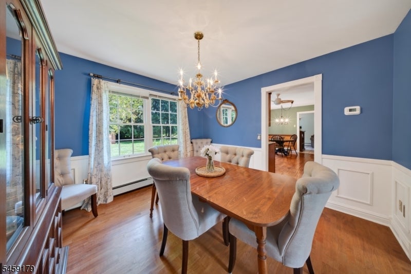 Blue dining room with a wooden table, upholstered chairs, chandelier, and large garden-facing window.