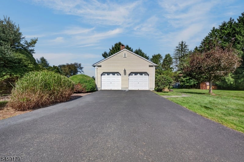 Detached two-car garage at the end of a broad paved driveway, bordered by shrubs and lawn.