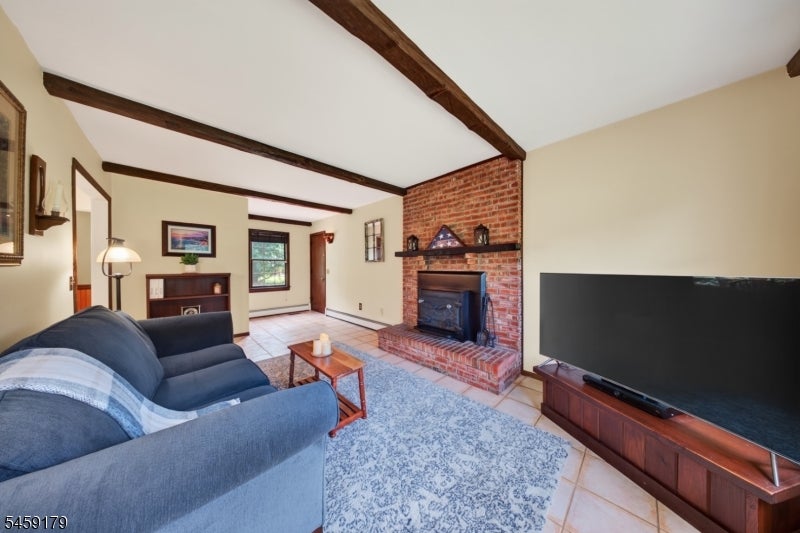 Living room with exposed ceiling beams, brick fireplace, blue sofa, and large television.