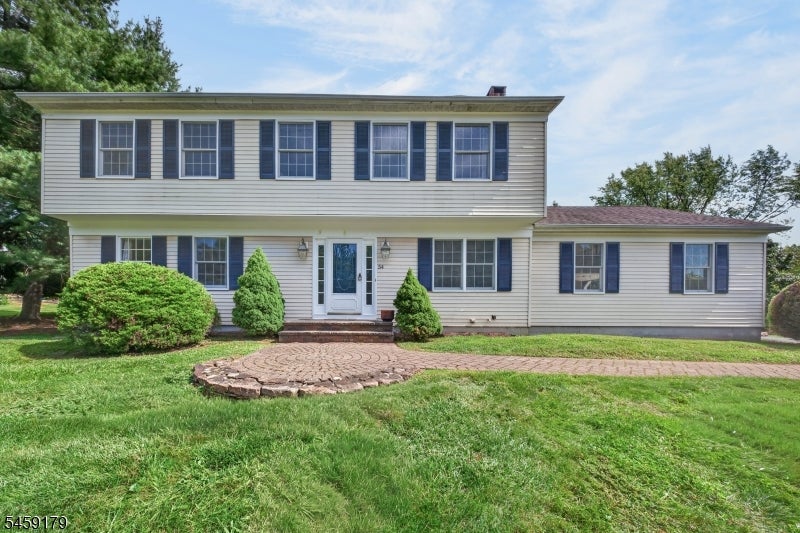 Two-story house with blue shutters, a broad lawn, and a circular brick walkway.