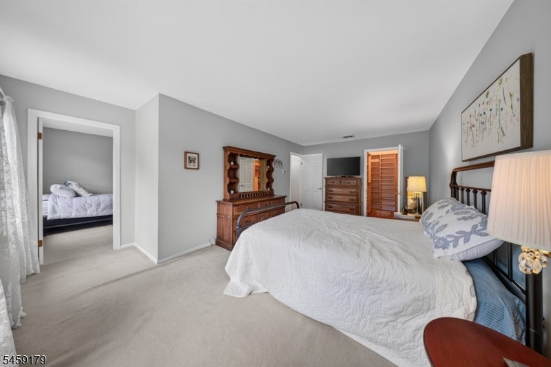 Furnished bedroom with white bedding, dark wood furniture, and an open doorway to another bedroom.