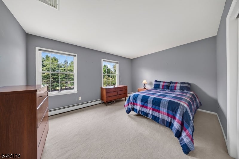 Bedroom with gray walls, two windows, wooden dressers, and a bed with blue and red plaid bedding.