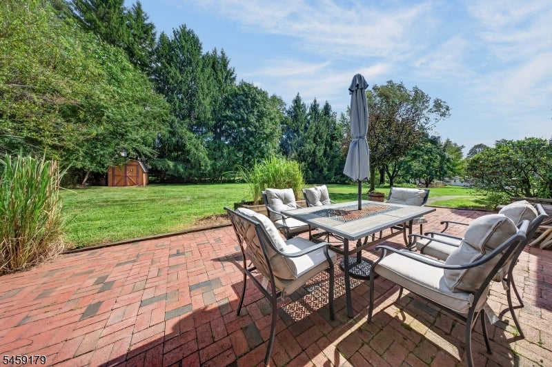 Brick backyard patio with an outdoor dining set, closed umbrella, and expansive lawn.
