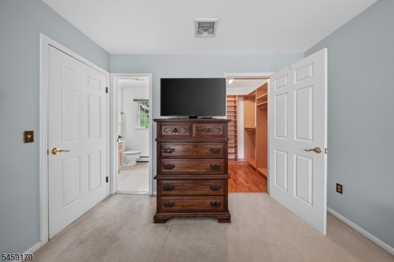 Bedroom with a dark wood dresser and television between open bathroom and closet doors.