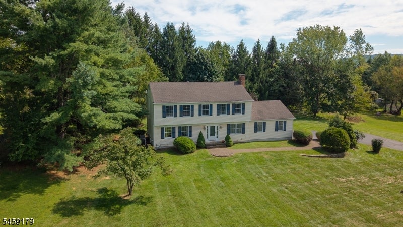 Two-story house with dark shutters, a broad mowed lawn, and mature trees around the property.