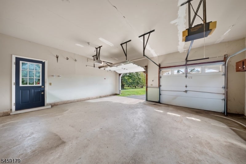 Empty garage with a concrete floor, blue side door, and open view onto the lawn.