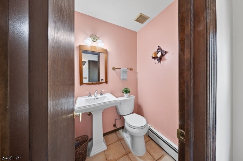 Pink bathroom with a pedestal sink, toilet, wood-framed mirror, and tan tile floor.
