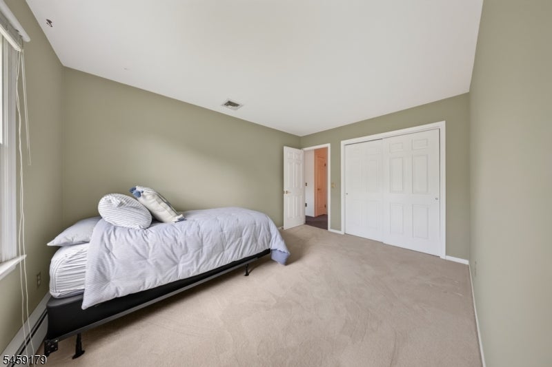 Bedroom with white bedding, muted green walls, beige carpet, and white sliding closet doors.