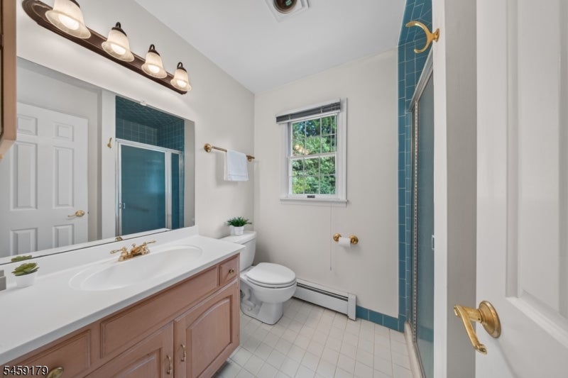 Bathroom with teal shower tile, wood vanity, and a window overlooking greenery.