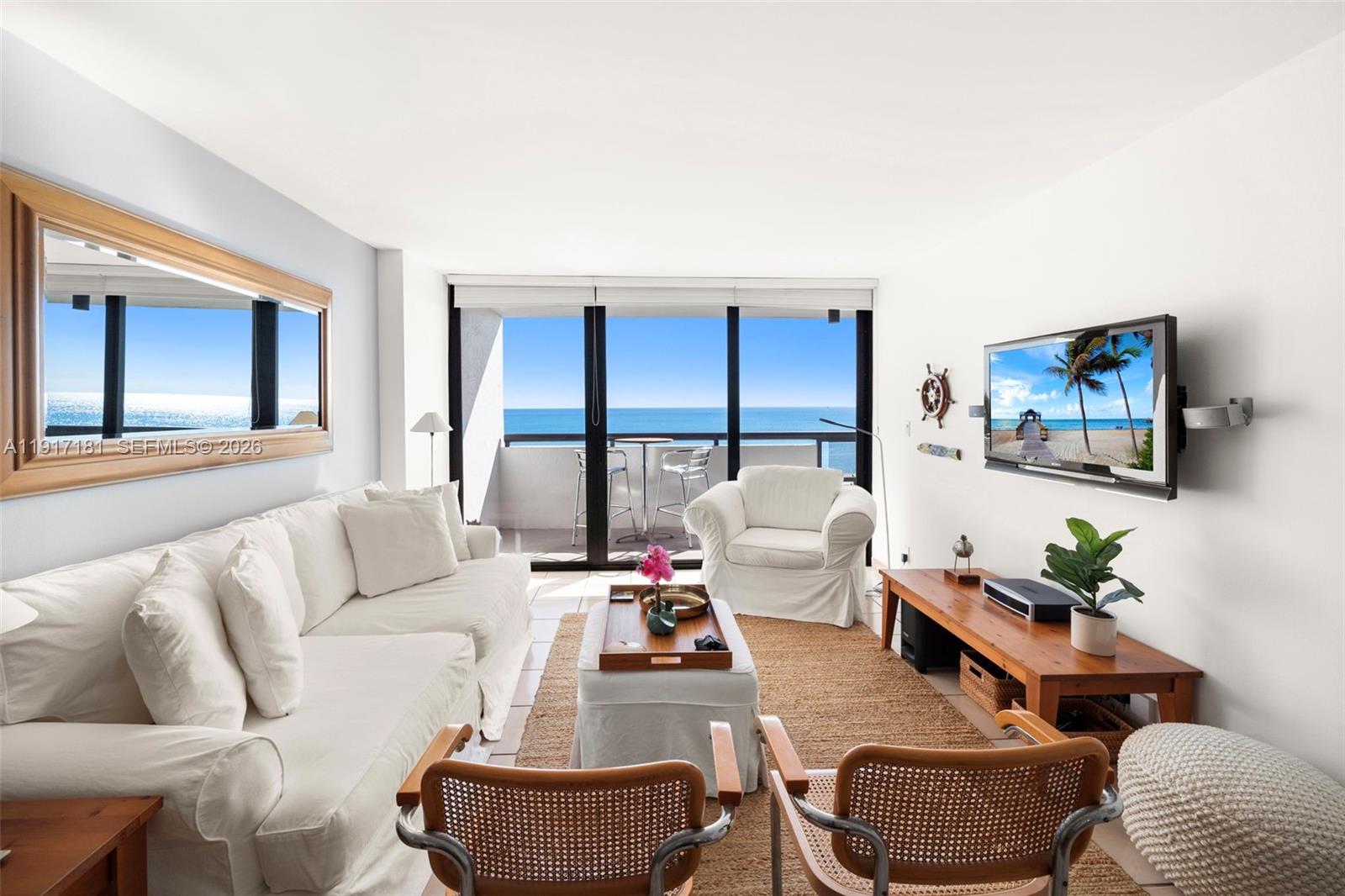 Furnished condo living room with white sofas and sliding doors overlooking the ocean.