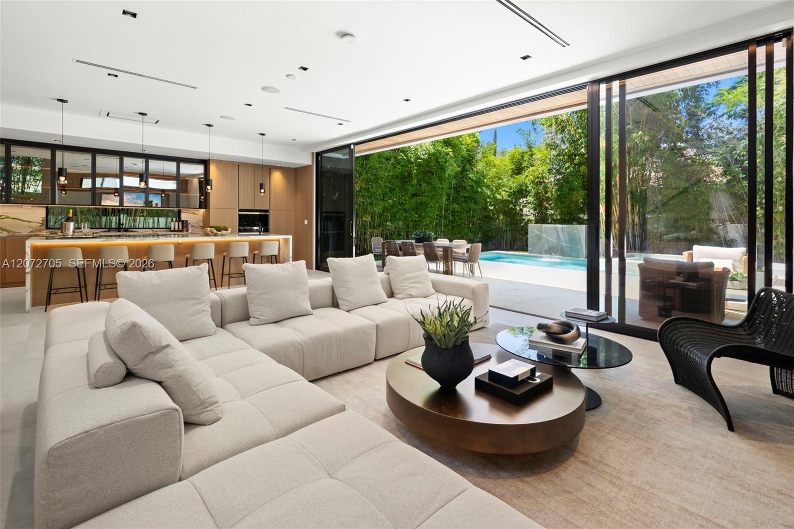 Modern living room with a cream sectional and floor-to-ceiling glass doors opening to a poolside patio.