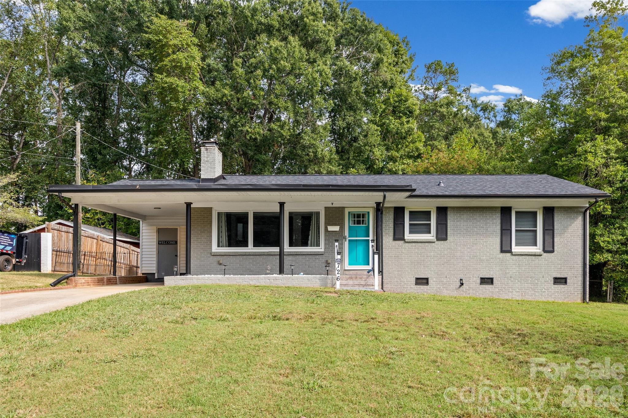 Gray brick single-story home with a turquoise front door, covered carport, and broad front lawn.