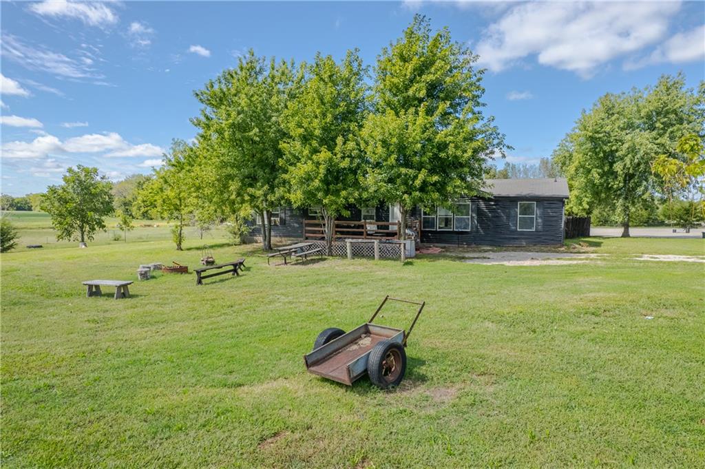 Single-story dark-sided house beneath large trees, with a wooden porch and broad grassy yard.