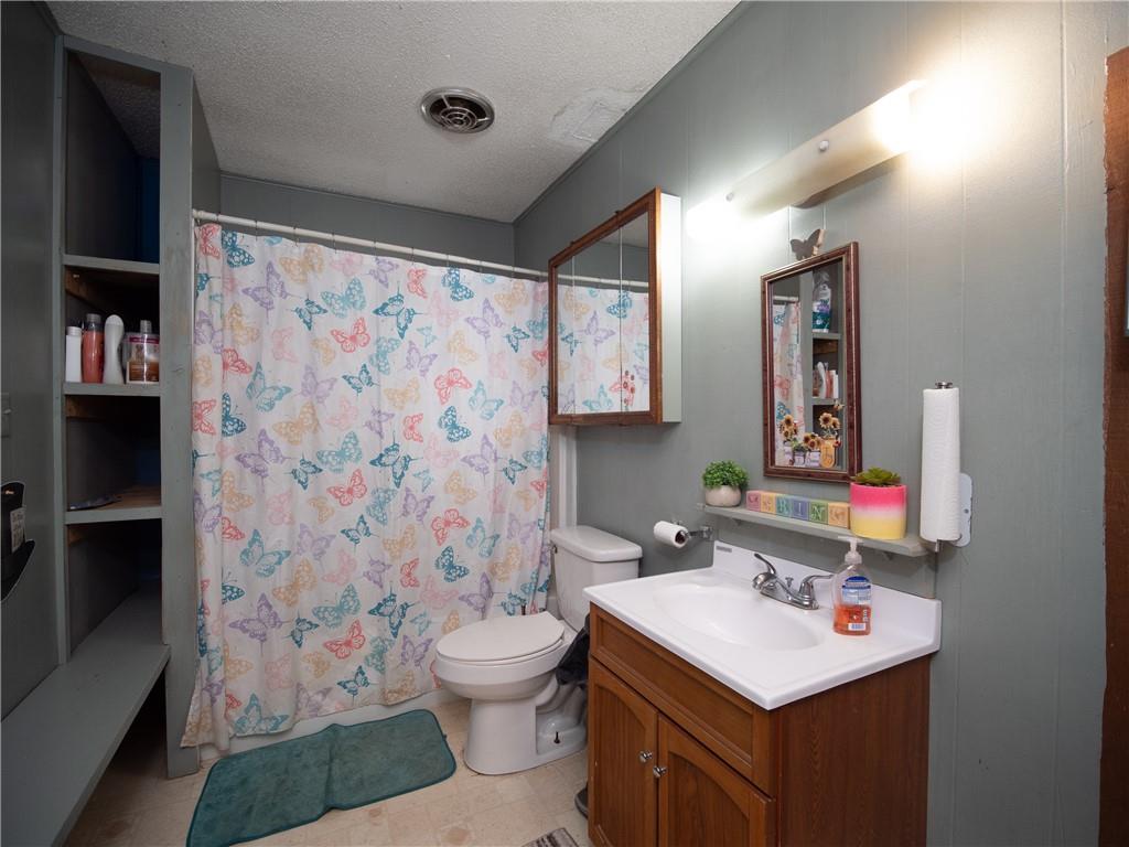 Bathroom with a butterfly-patterned shower curtain, toilet, and wooden vanity with a white sink.