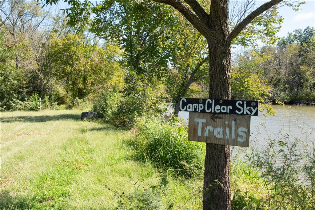 Grassy wooded riverbank with a tree-mounted Camp Clear Sky Trails sign.