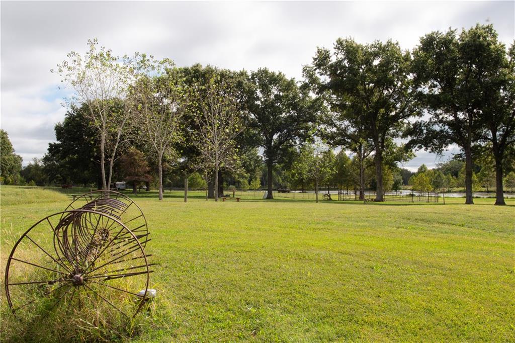 Grassy rural property with mature trees, a distant pond, and an old metal farm implement.