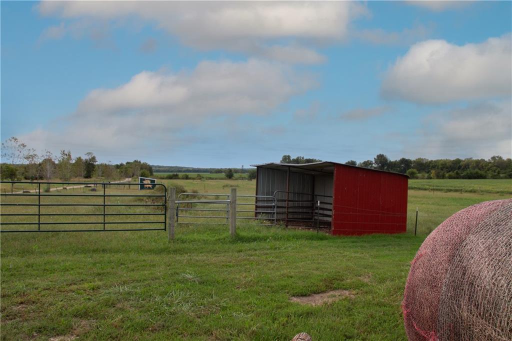 Fenced pasture with a red open shelter, metal gates, and a round hay bale.