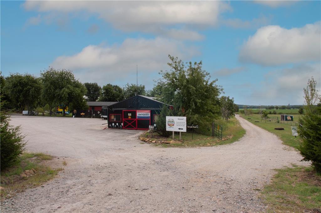 Roadside building with red trim and an antiques sign beside a gravel lane and open fields.