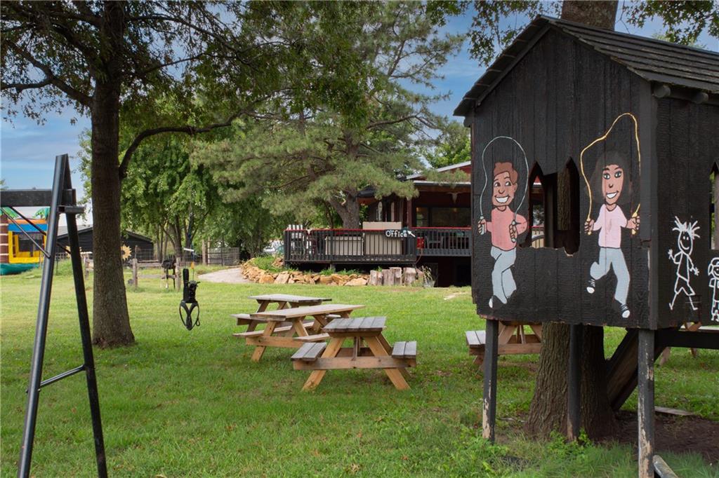 Outdoor grounds with picnic tables beneath trees and a painted play structure beside the office deck.