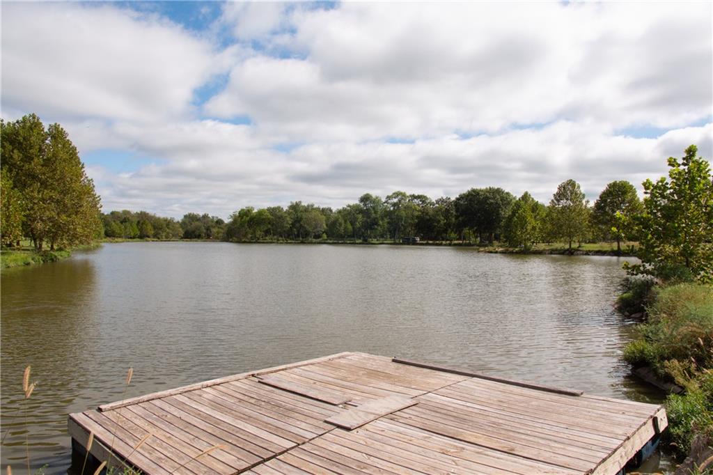 Wooden dock extending into a tree-lined pond beneath a cloudy sky.