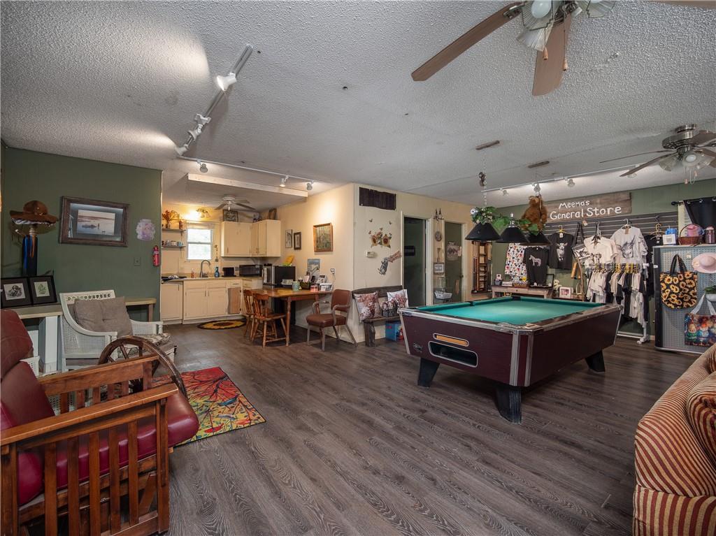 Furnished recreation room with a pool table, seating area, kitchen, and clothing racks.