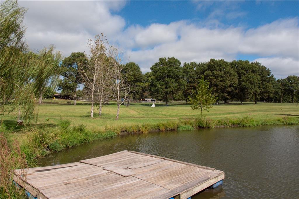 Wooden dock over a pond, facing a grassy lawn and tree line.
