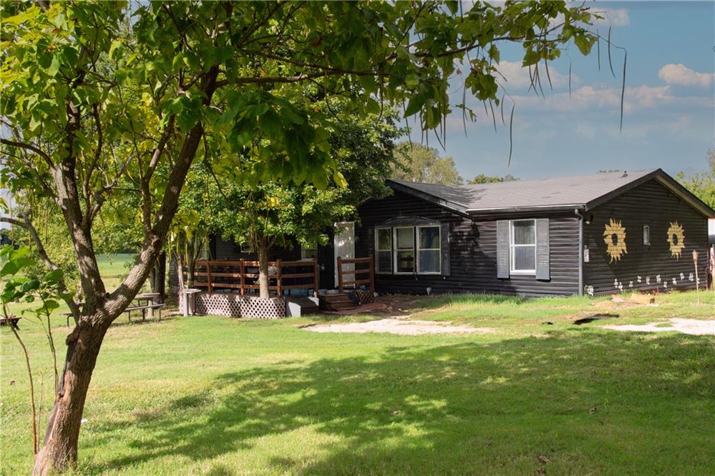 Dark-sided single-story home with a raised porch and sunflower wall decorations, shaded by a large tree.