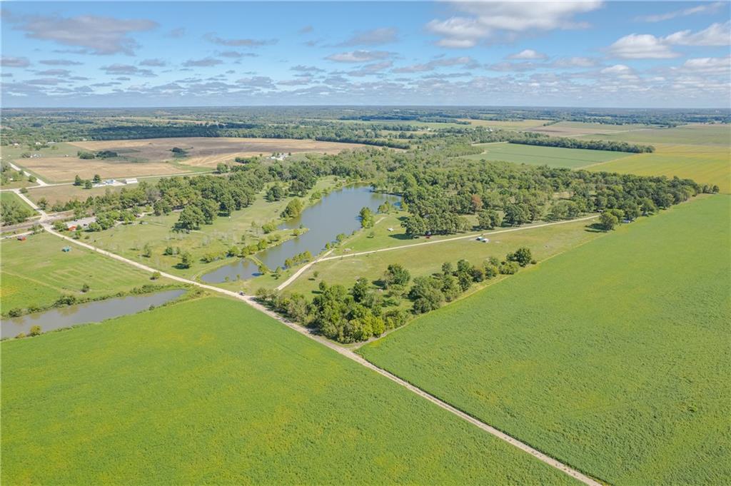 Aerial view of rural acreage with a pond, tree-lined fields, and gravel roads.