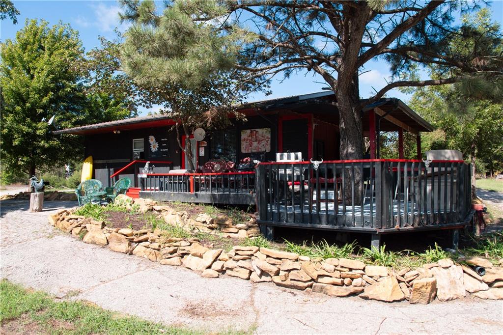 Dark single-story home with red trim and a large deck shaded by mature trees.