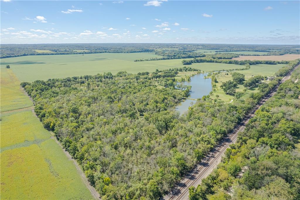 Aerial view of wooded acreage with a pond and railroad tracks beside surrounding farmland.