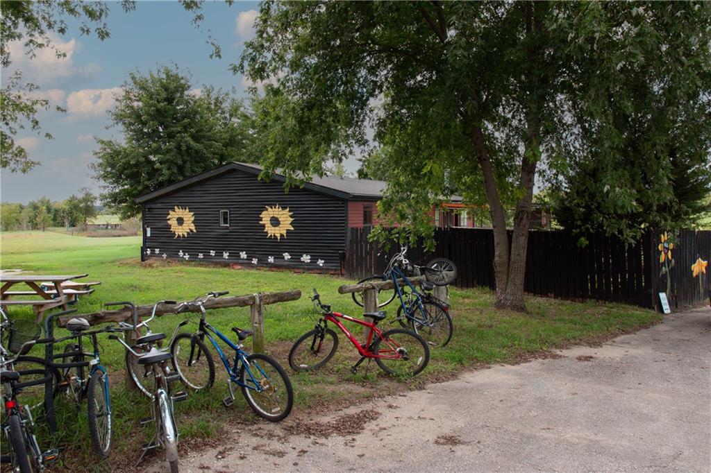 Dark-sided building with yellow flower decorations behind a fence, with bicycles parked along a wooden rail.