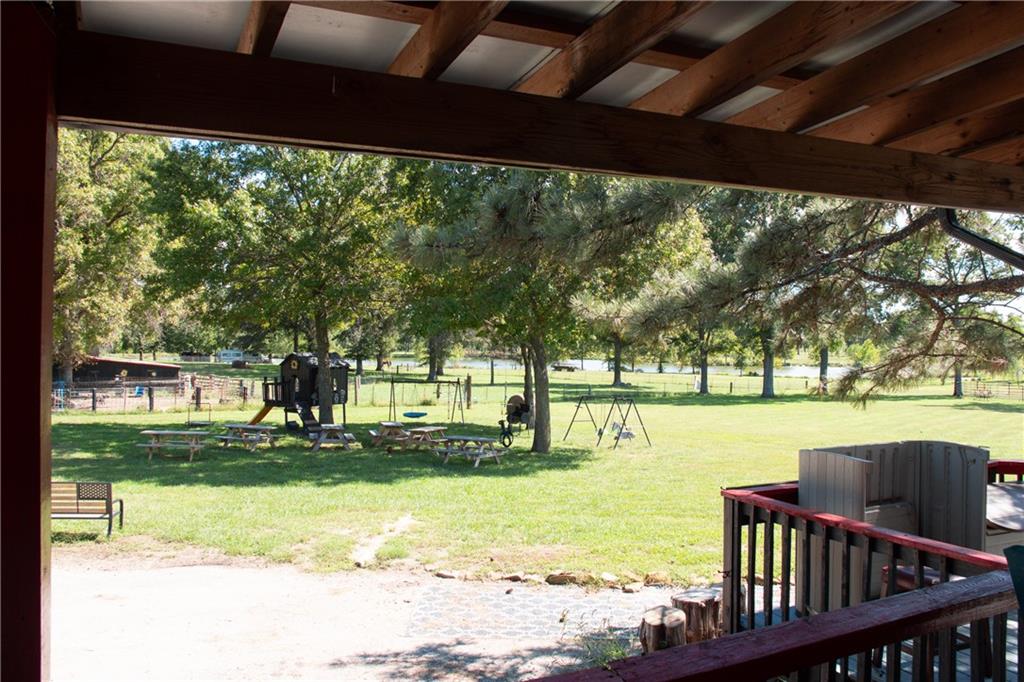 Backyard lawn with mature trees, picnic tables, and playground, viewed from a covered porch.