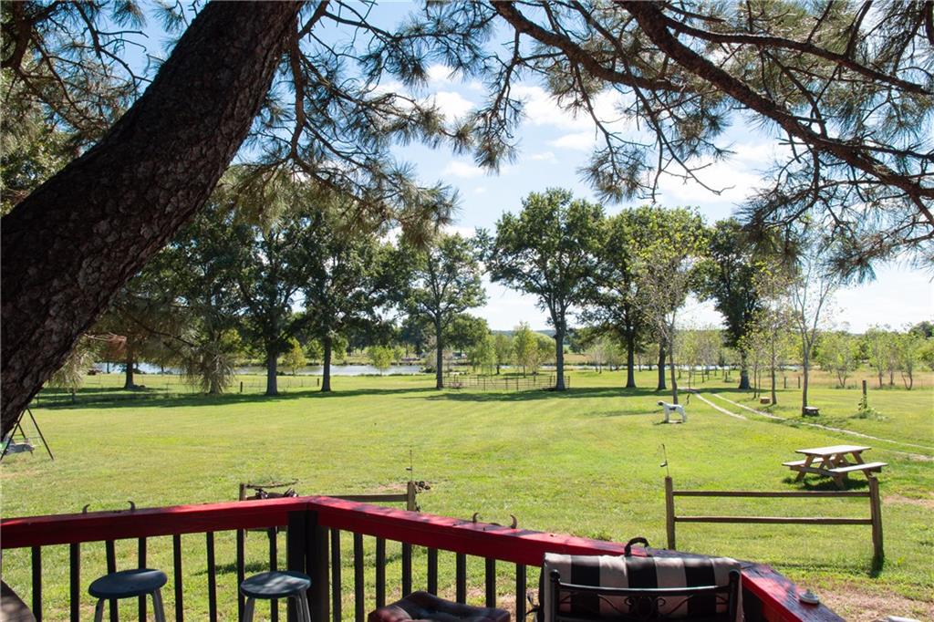 Expansive grassy yard viewed from a red-railed deck, with mature trees, pond, and picnic table.