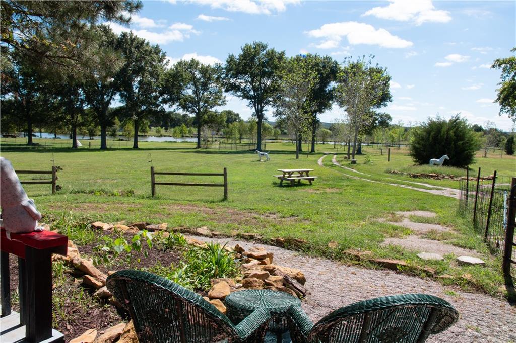 Grassy backyard with a distant pond, mature trees, and woven patio chairs.