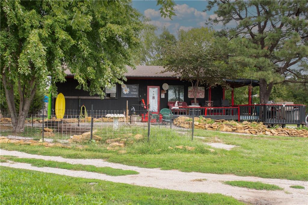 Dark-sided home with a red-railed porch, shaded by mature trees beside a grassy yard.