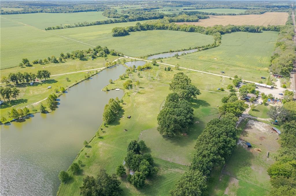 Aerial view of a rural property with a large pond, open fields, and mature trees.