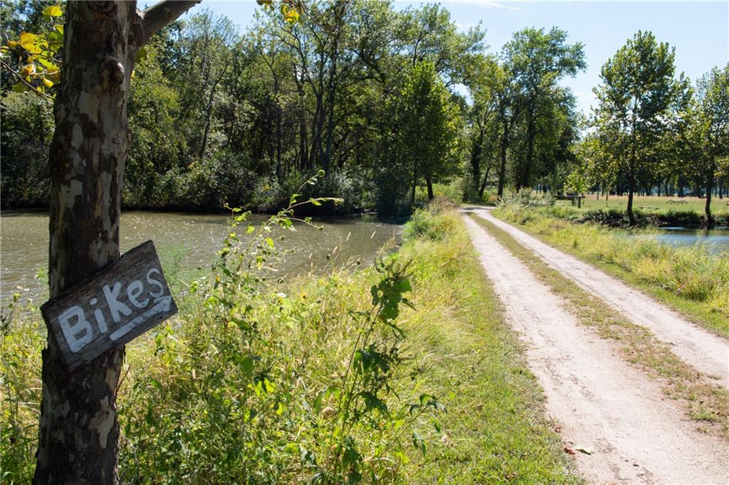 Gravel path between ponds and trees, with a wooden “Bikes” sign on a nearby tree.