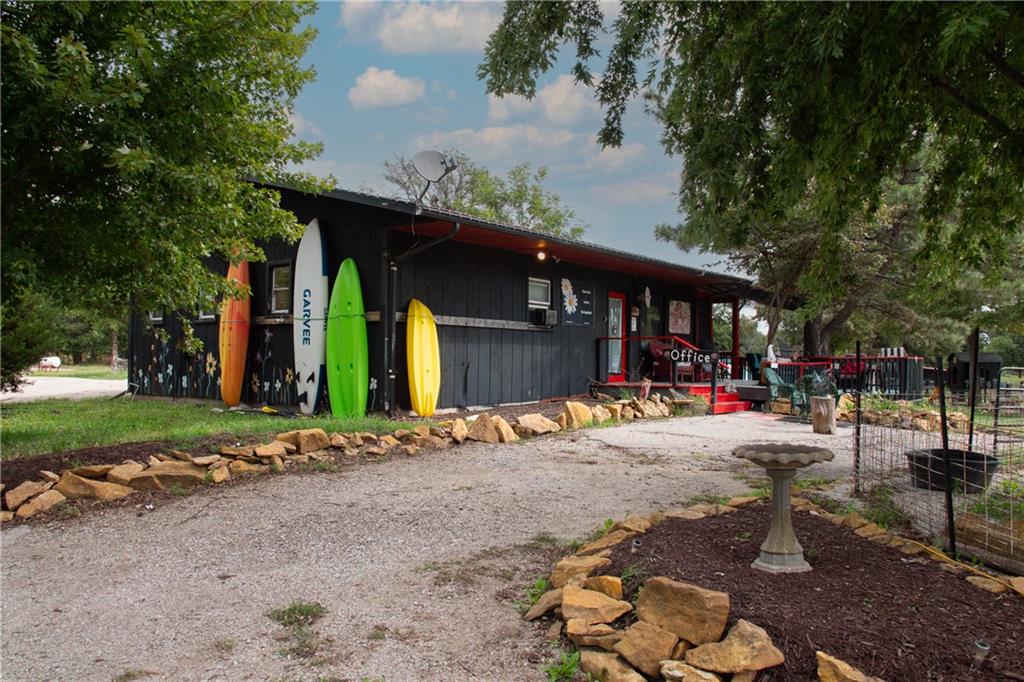 Dark office building with red trim, colorful surfboards, and a gravel drive beneath mature trees.