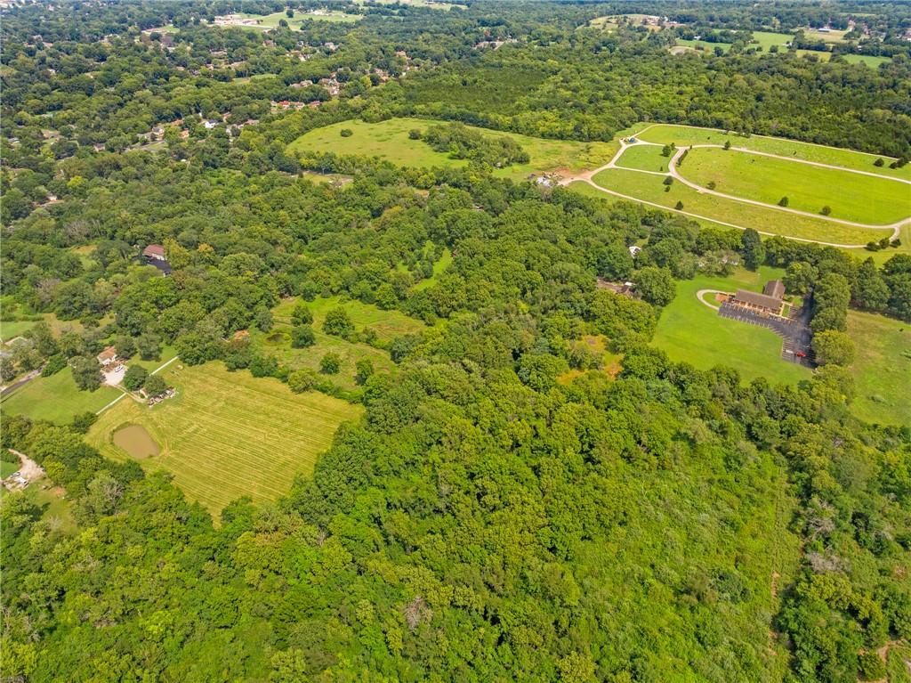 Aerial view of wooded property with open fields, a small pond, and scattered nearby buildings.