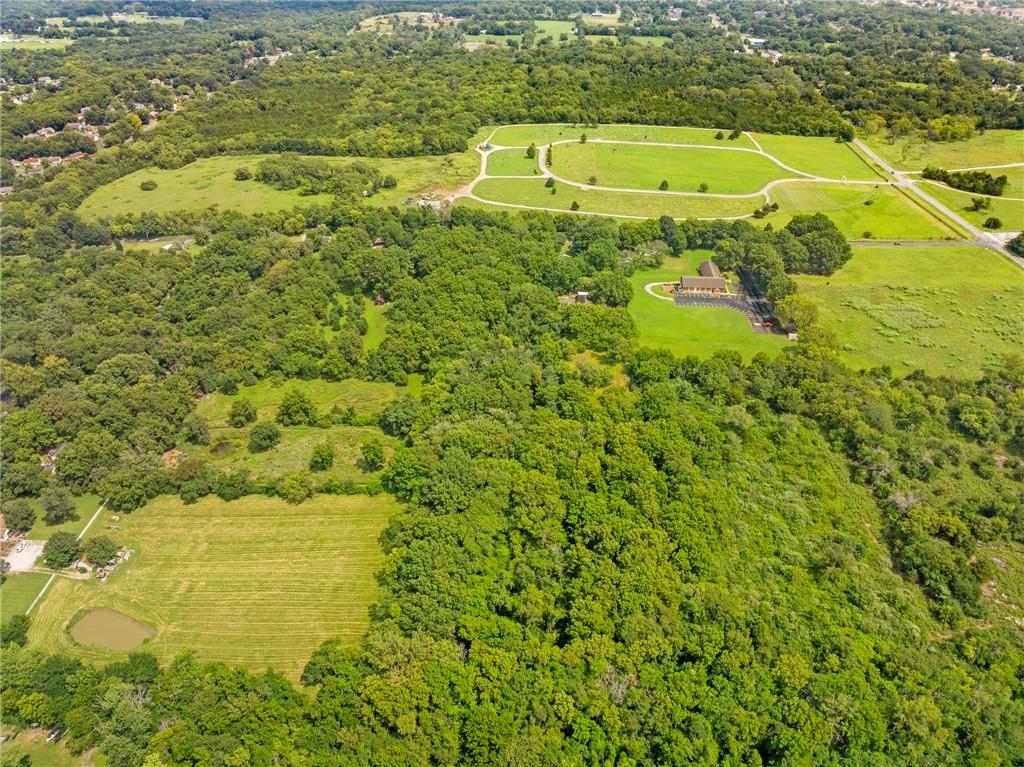 Aerial view of wooded land, open fields, a small pond, and winding paved paths.