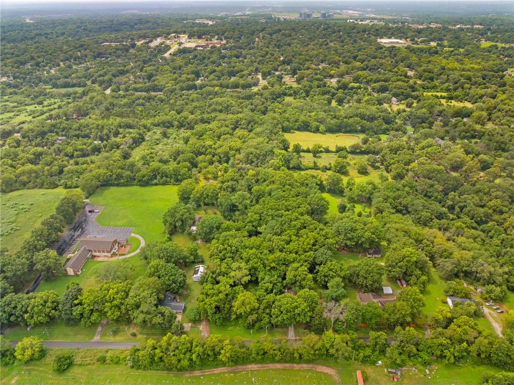 Aerial view over wooded land, scattered homes, open fields, and a distant city skyline.